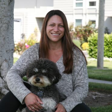 Dr Erin Bukofsky sitting on the ground with a dog